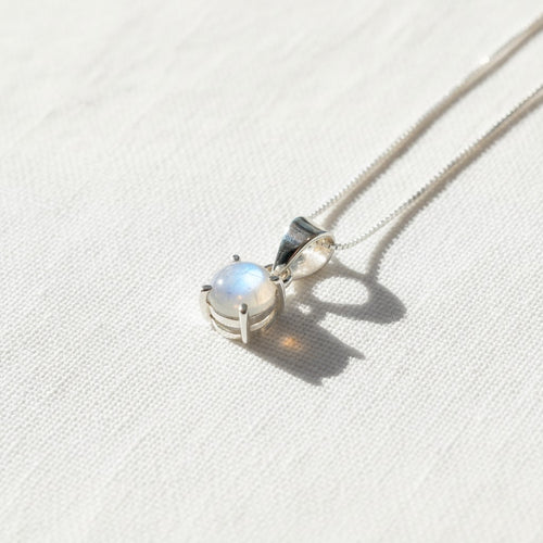 Astral Moonstone Round Necklace - Sterling Silver, a sterling silver pendant necklace featuring a round bezel-set moonstone gemstone with an iridescent glow, resting on a textured off-white fabric surface.