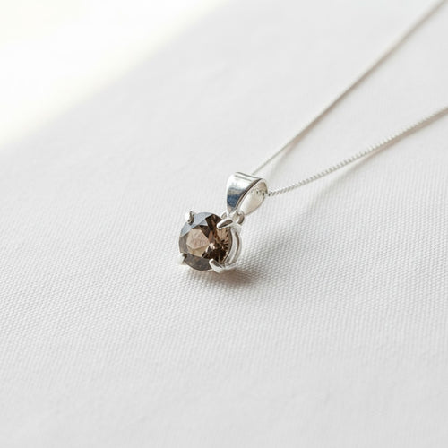 Astral Smoky Quartz Round Necklace - Sterling Silver, a silver pendant necklace featuring a round smoky brown quartz gemstone in a four-prong setting, resting on a textured white fabric surface.