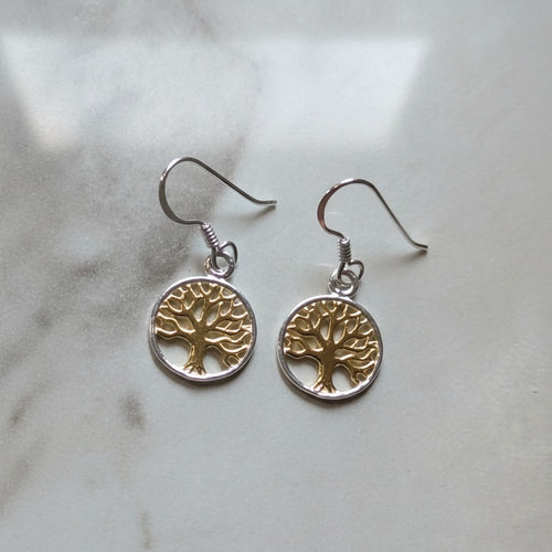 Auryn Tree of Life Drop Earrings - Sterling Silver & Gold Plate, a pair of tree of life drop earrings with gold and silver metal detailing, resting on a light marble surface.