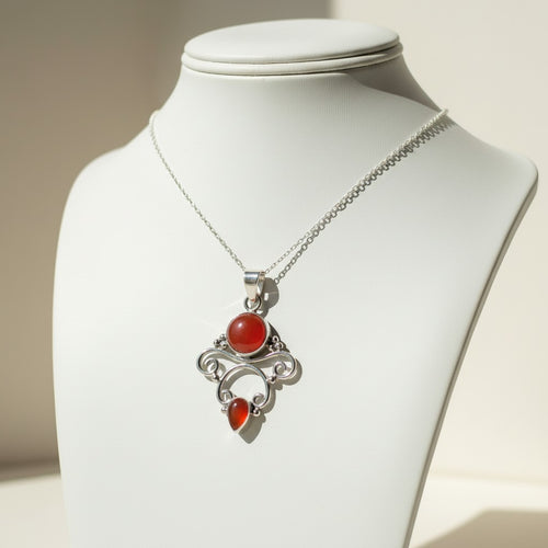 Awen Carnelian Necklace - Sterling Silver, a silver pendant necklace with a round red gemstone and a smaller teardrop red gemstone, displayed on a white jewellery bust.