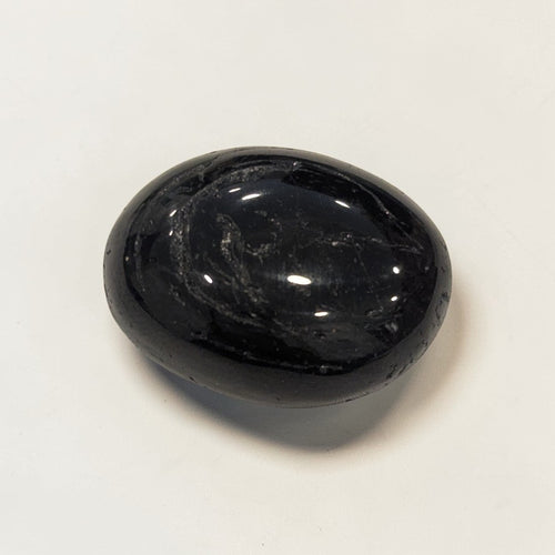 Black Tourmaline Tumble Stone - Polished, smooth polished black stone on a white background.