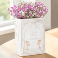 White Book Shaped Vase - Good Vibes, book-shaped ceramic vase filled with pink and white flowers on a wooden table.