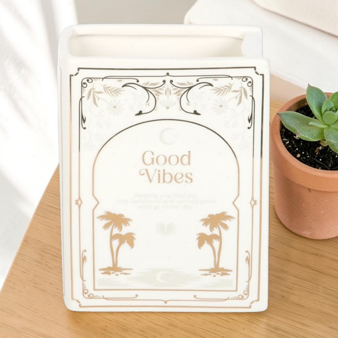 White Book Shaped Vase - Good Vibes, empty book-shaped ceramic vase beside a small potted succulent plant on a wooden surface.