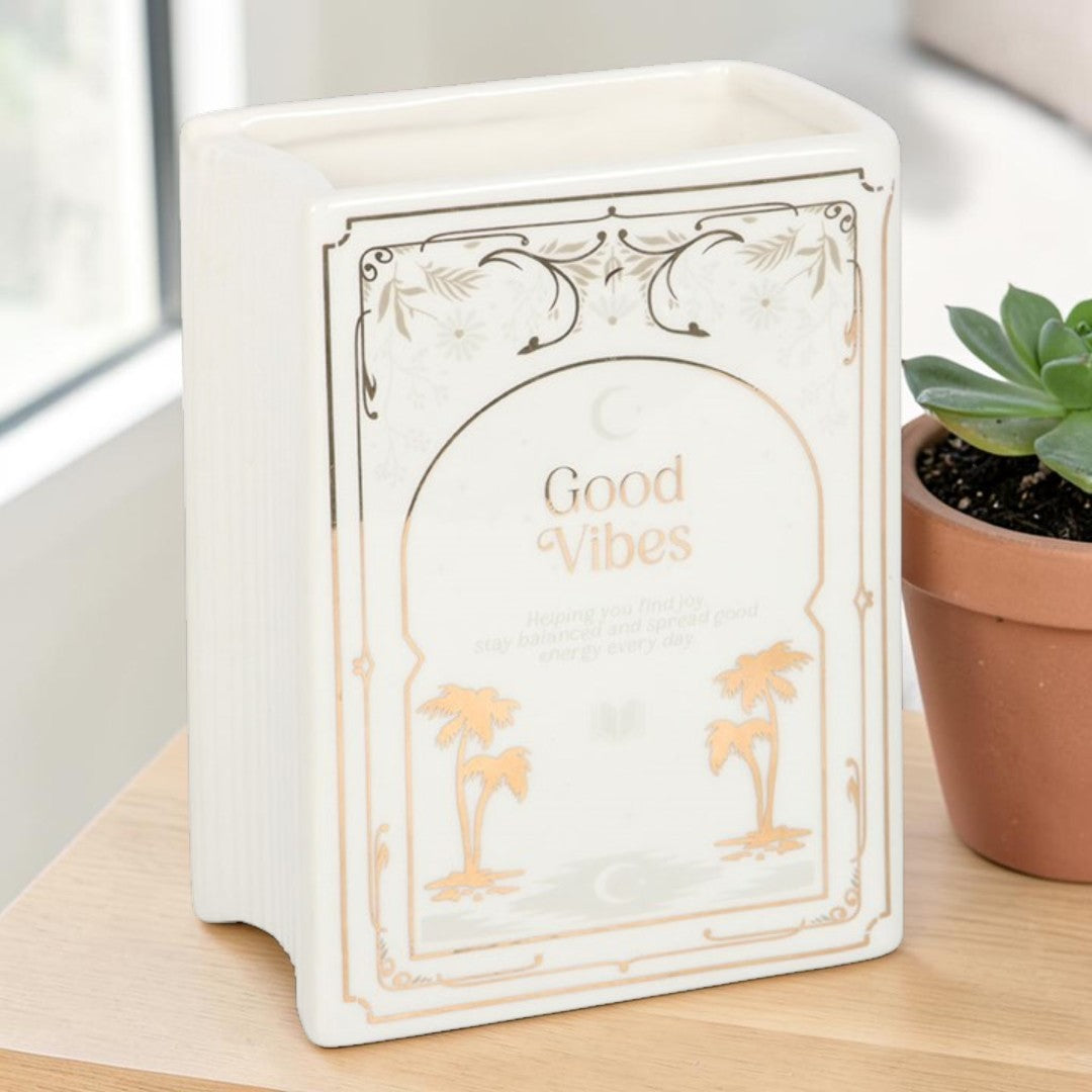 White Book Shaped Vase - Good Vibes, close-up side view of the white ceramic book-shaped vase with a small potted succulent plant beside it on a wooden surface.